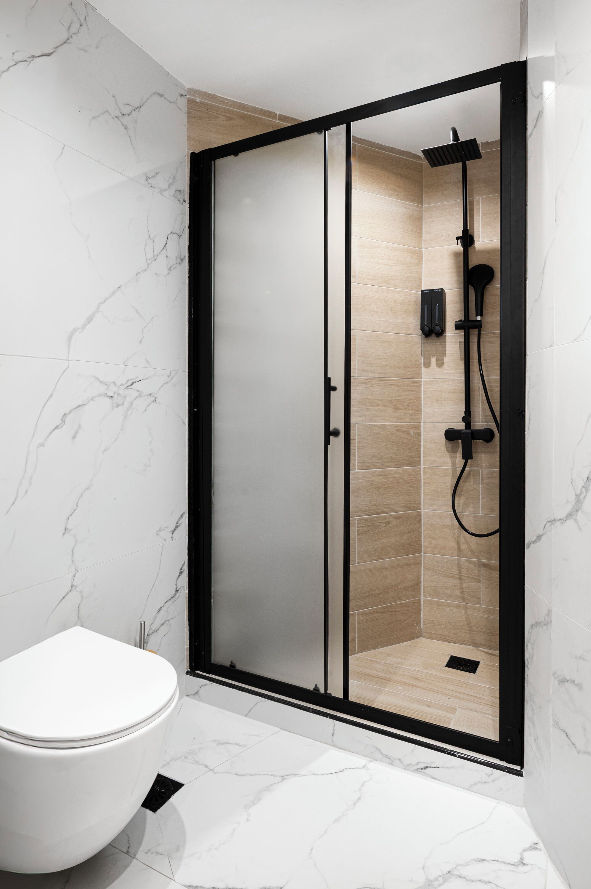 A modern bathroom with a glass-enclosed shower, a white toilet, and marble flooring.
