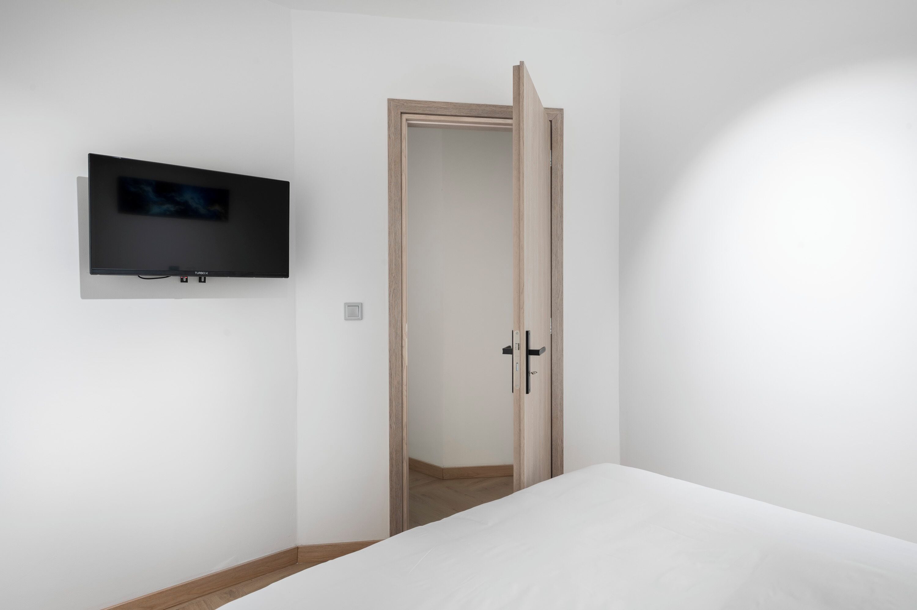 Una habitación con una cama, un televisor montado en la pared y un armario de madera con puerta.