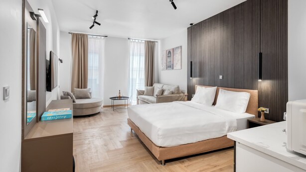 A modern hotel room with a large bed, a sofa, a small table, and a desk. - Athenian Heart Suites  (Athens)