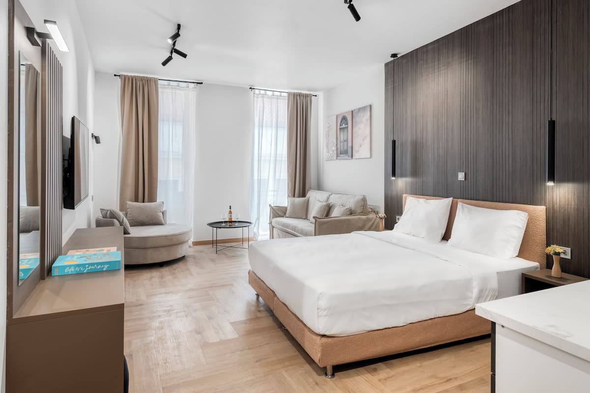 A modern hotel room with a large bed, a sofa, a small table, and a desk.