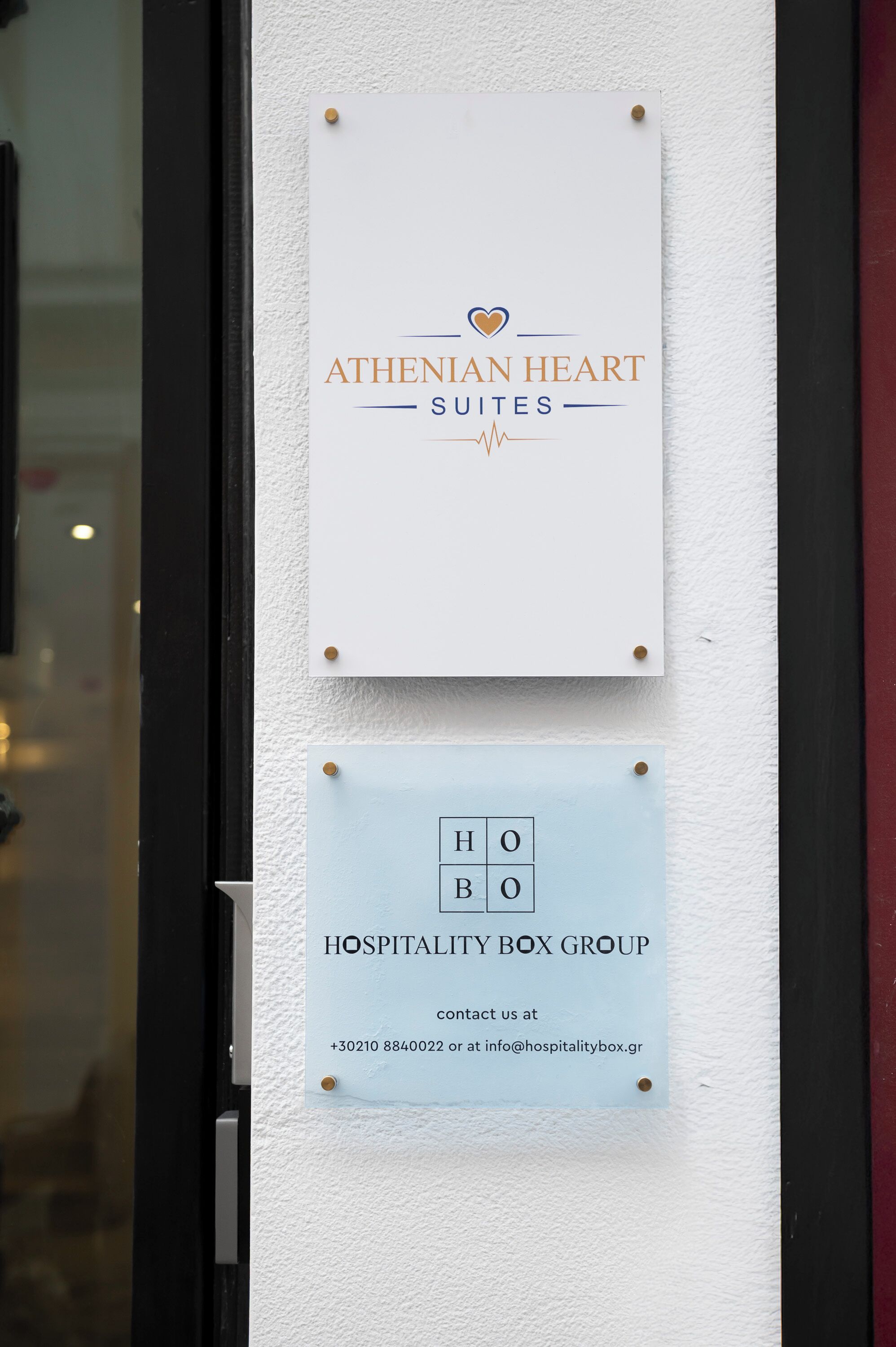 Zwei Schilder: 'ATHENIAN HEART SUITES' und 'HOSPITALITY BOX GROUP' mit Kontaktinformationen.