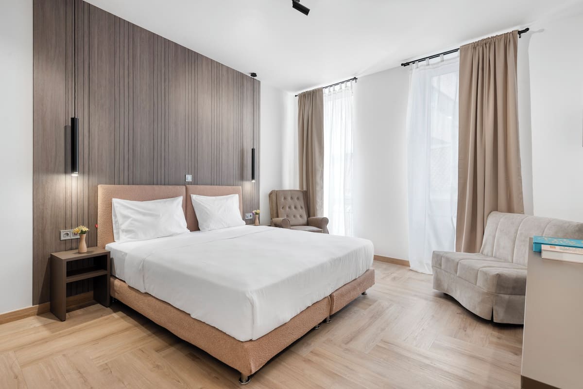 A modern hotel room with a large bed, a chair, a nightstand, and a wooden accent wall.