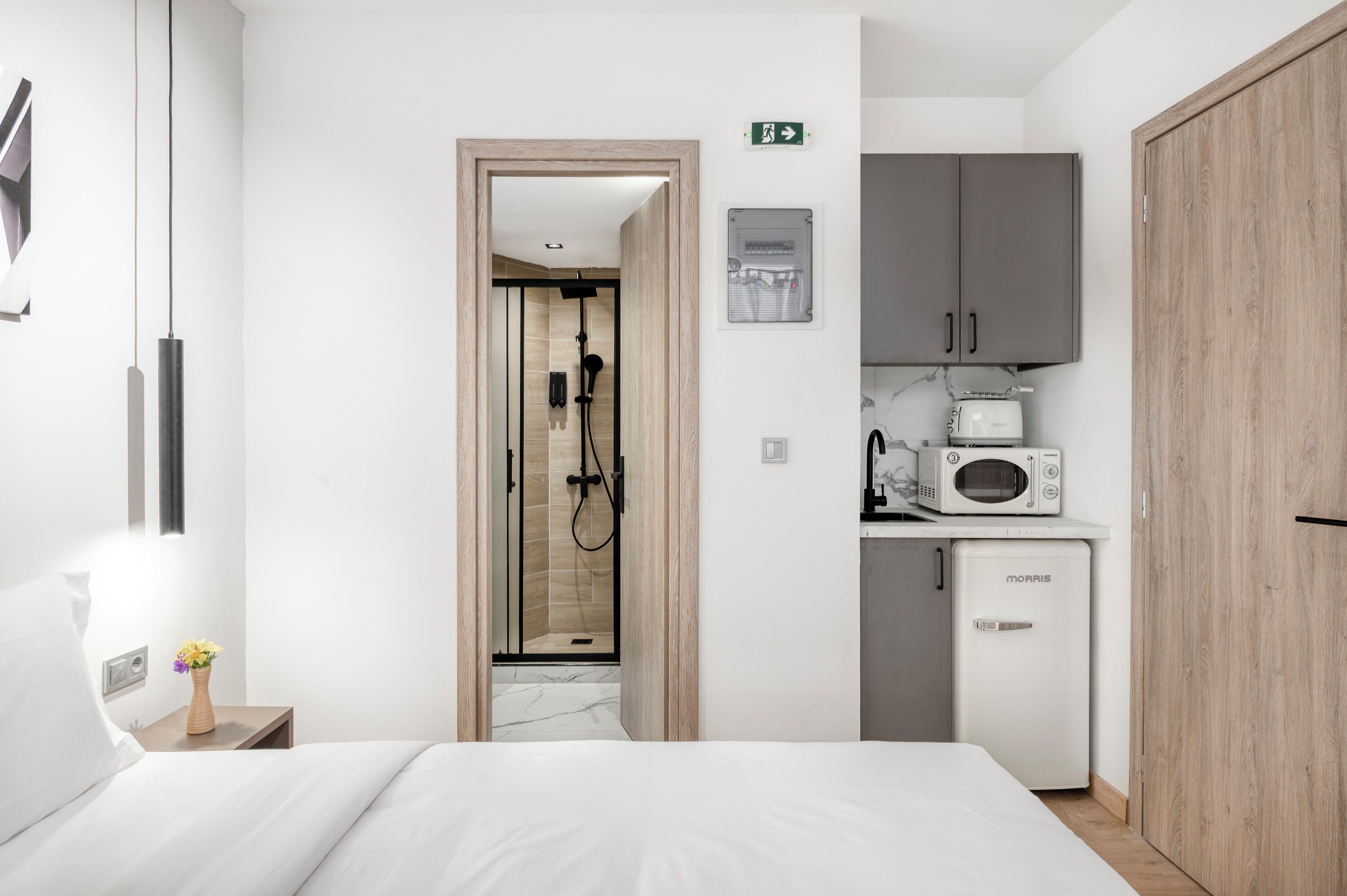 A modern hotel room with a bed, a shower, a microwave, and a refrigerator.