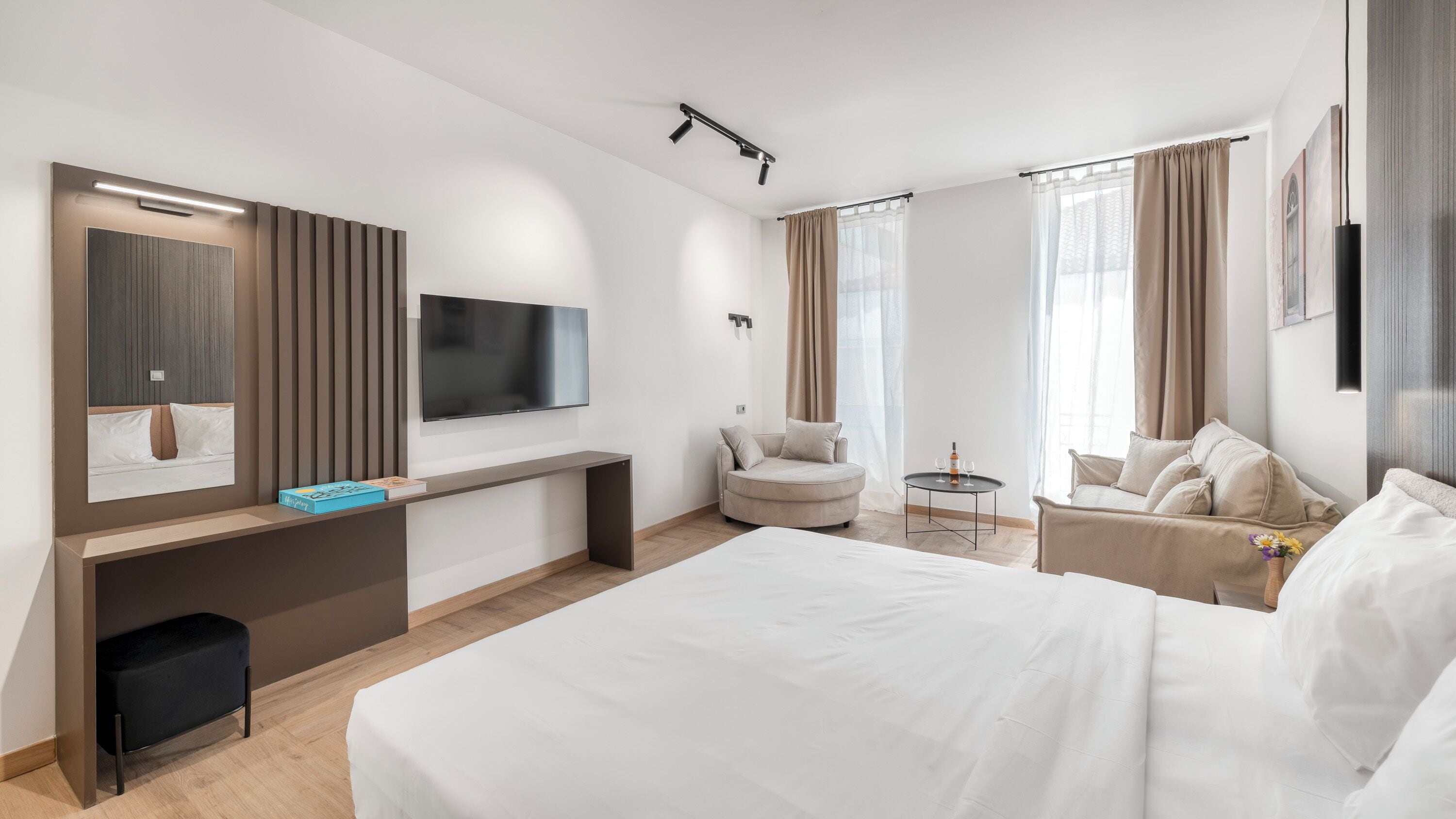 A hotel room with a bed, a desk, a TV, a chair, and a small table with a bottle and glasses.