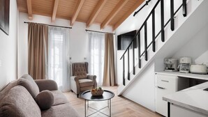 A modern living room with a sofa, a chair, a small table with fruit, a kitchen area with appliances, and a staircase. - Athenian Heart Suites  (Athens)