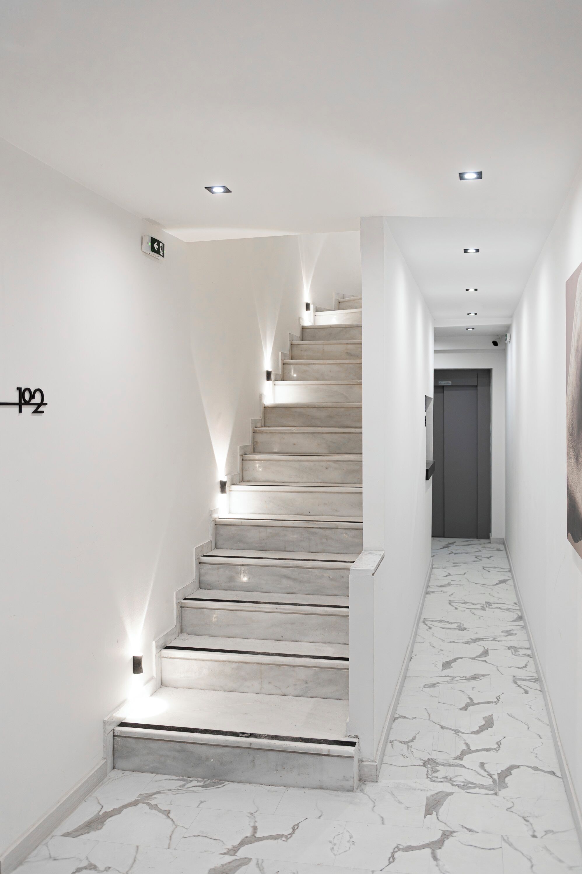 A modern staircase with marble steps and walls, a number '102' sign, and recessed lighting.