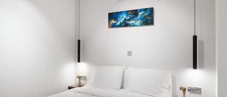 Una habitación de hotel moderna con cama, paredes blancas, aire acondicionado, un cuadro y lámparas de noche.