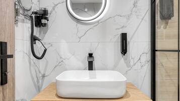A bathroom with a marble wall, a wooden vanity, a round mirror, a handheld showerhead, and a towel hanging on a rack.