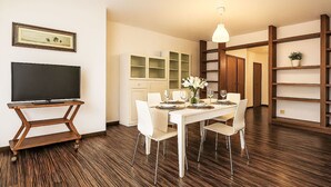 Een eetgedeelte met een witte tafel, stoelen en een televisie op een houten standaard.