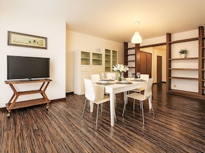 Un coin repas avec une table blanche, des chaises et un téléviseur posé sur un meuble en bois.