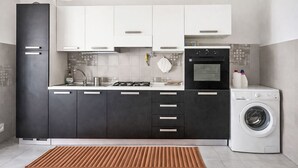 Een moderne keuken met zwarte kastjes, een roestvrijstalen koelkast, een gasfornuis, een oven en een ingebouwde wasmachine.