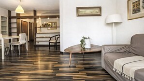 Een moderne woonkamer met een bank, een eettafel met stoelen, een bijzettafel met een plant en een ingelijst schilderij aan de muur.