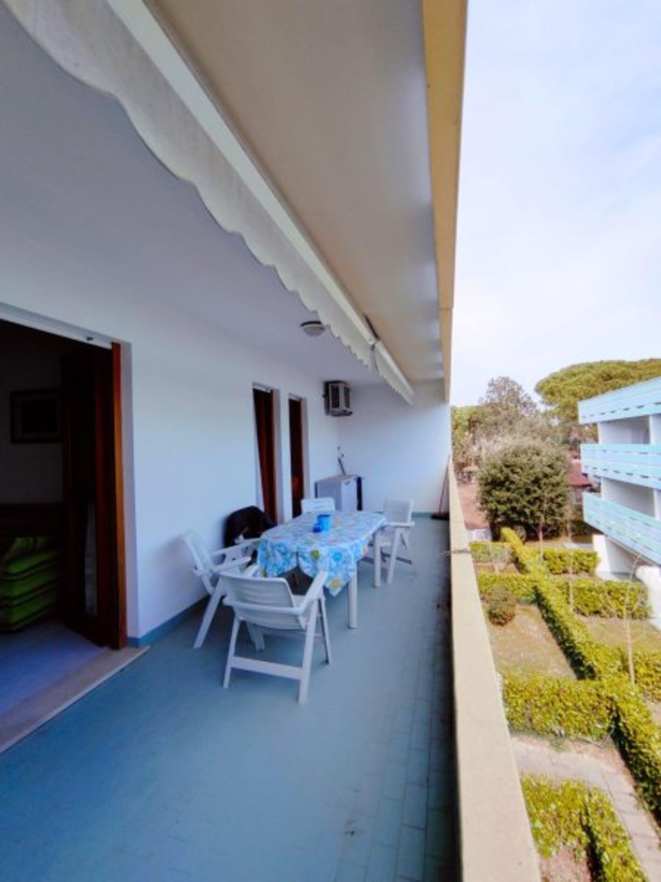 Un balcon avec une table et des chaises, un petit climatiseur et une vue sur un immeuble et des espaces verts.