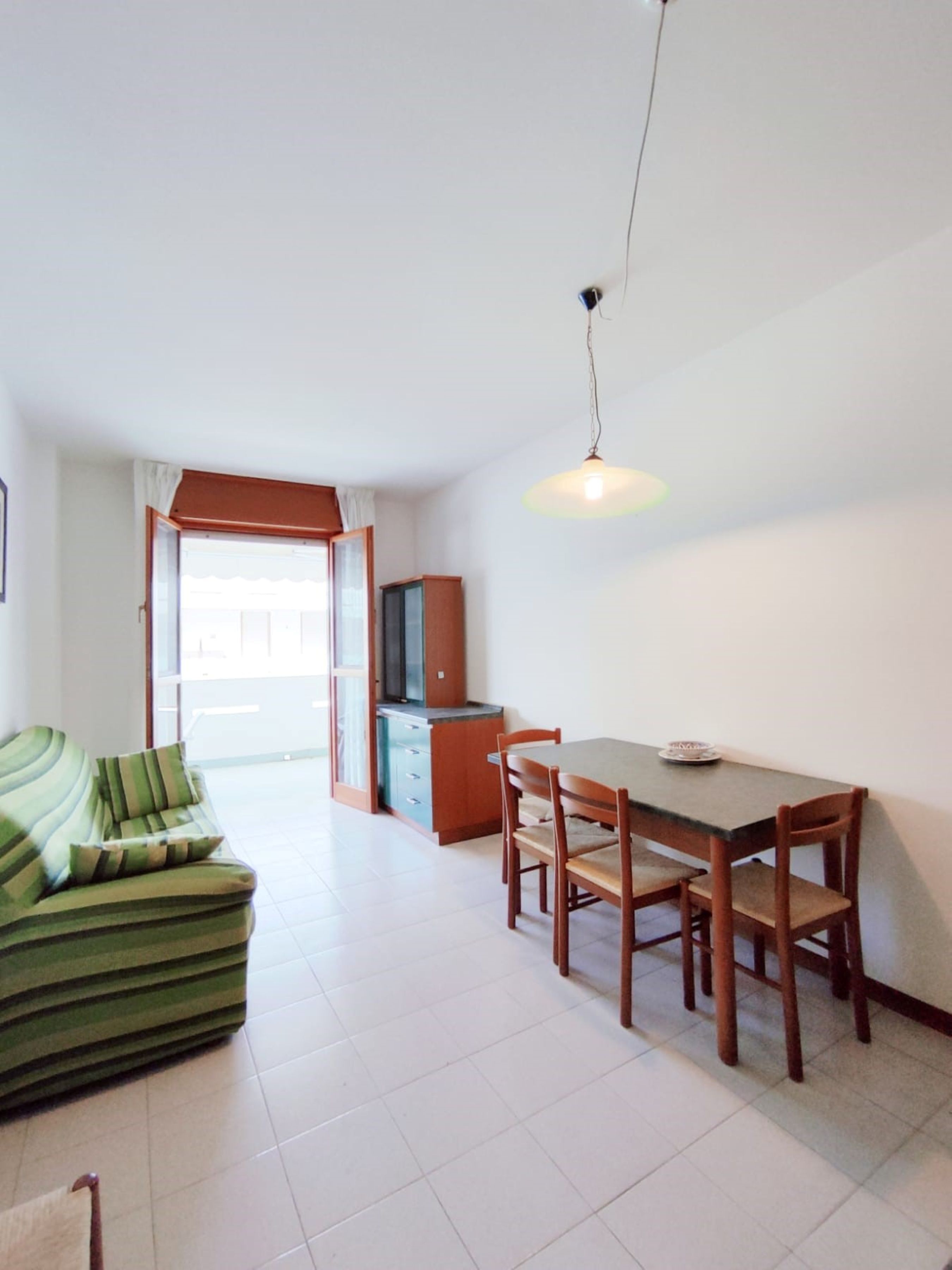 A dining area with a table and chairs, a green sofa, a cabinet, and a television.