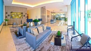 A modern lobby with a grey sofa, a reception desk, and a large window offering a view of the outdoors. - Modern 1BR Condo in BGC One Uptown Near Uptown Mall Landers Mitsukoshi Mall Wifi (Taguig)