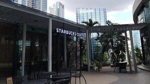 An outdoor Starbucks coffee shop with tables and chairs, surrounded by tall buildings and a cloudy sky. - Modern 1BR Condo in BGC One Uptown Near Uptown Mall Landers Mitsukoshi Mall Wifi (Taguig)
