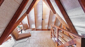 A cozy attic bedroom with a sloped ceiling, a wooden staircase, a comfortable chair, and a small table with a plant. - White Oak Hollow - newly updated (Innsbrook)