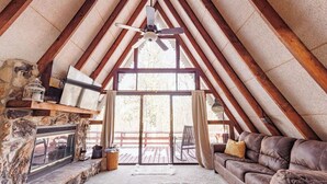 A cozy attic room with a stone fireplace, a leather couch, and a large window overlooking a deck. - White Oak Hollow - newly updated (Innsbrook)