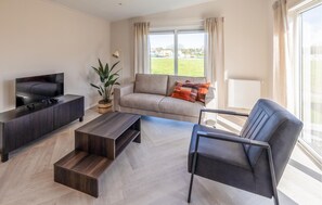 Un salon moderne avec un téléviseur à écran plat, un canapé, une table basse et un fauteuil.