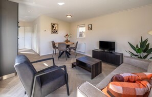 Un salon moderne comprenant un canapé, un fauteuil, une table basse, un téléviseur et un coin repas avec des chaises et une table.