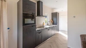 Una cocina moderna con armarios oscuros, horno empotrado y campana extractora de acero inoxidable.