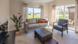 Una sala de estar moderna con sofá, sillón, mesa de centro y televisor.