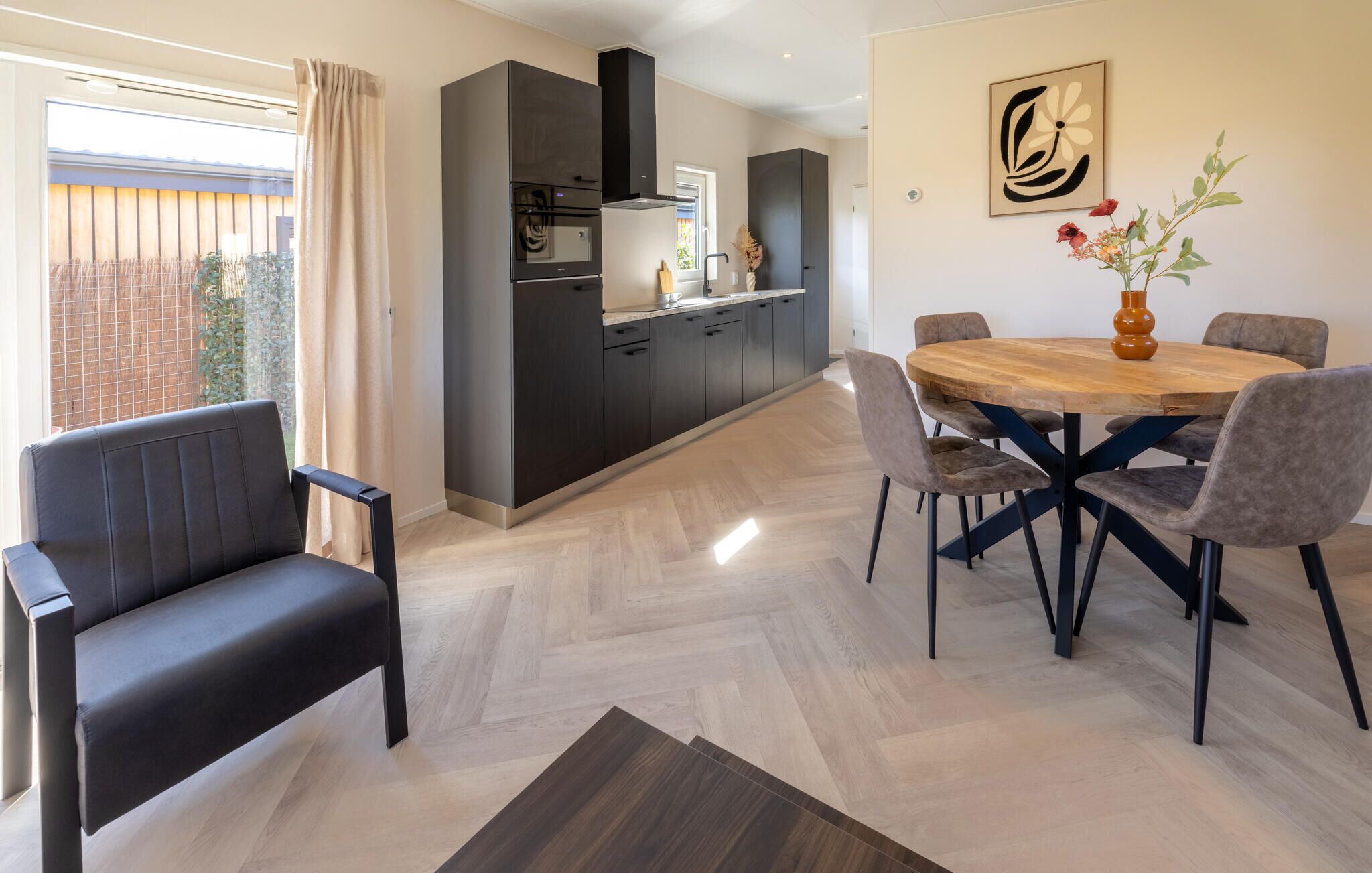 Une cuisine moderne avec des meubles de couleur sombre, un îlot central et un coin repas comprenant une table ronde en bois et des chaises.
