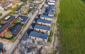Vista aérea de uma área residencial com várias casas de dois andares, uma rua pavimentada e um campo verde.