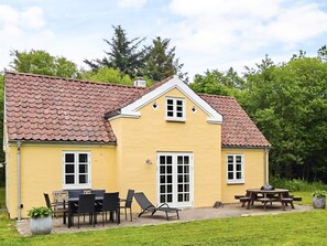 A yellow building with a red-tiled roof, a front door, and a patio with outdoor furniture. - 5 Star Holiday Home in Skagen (Skagen)