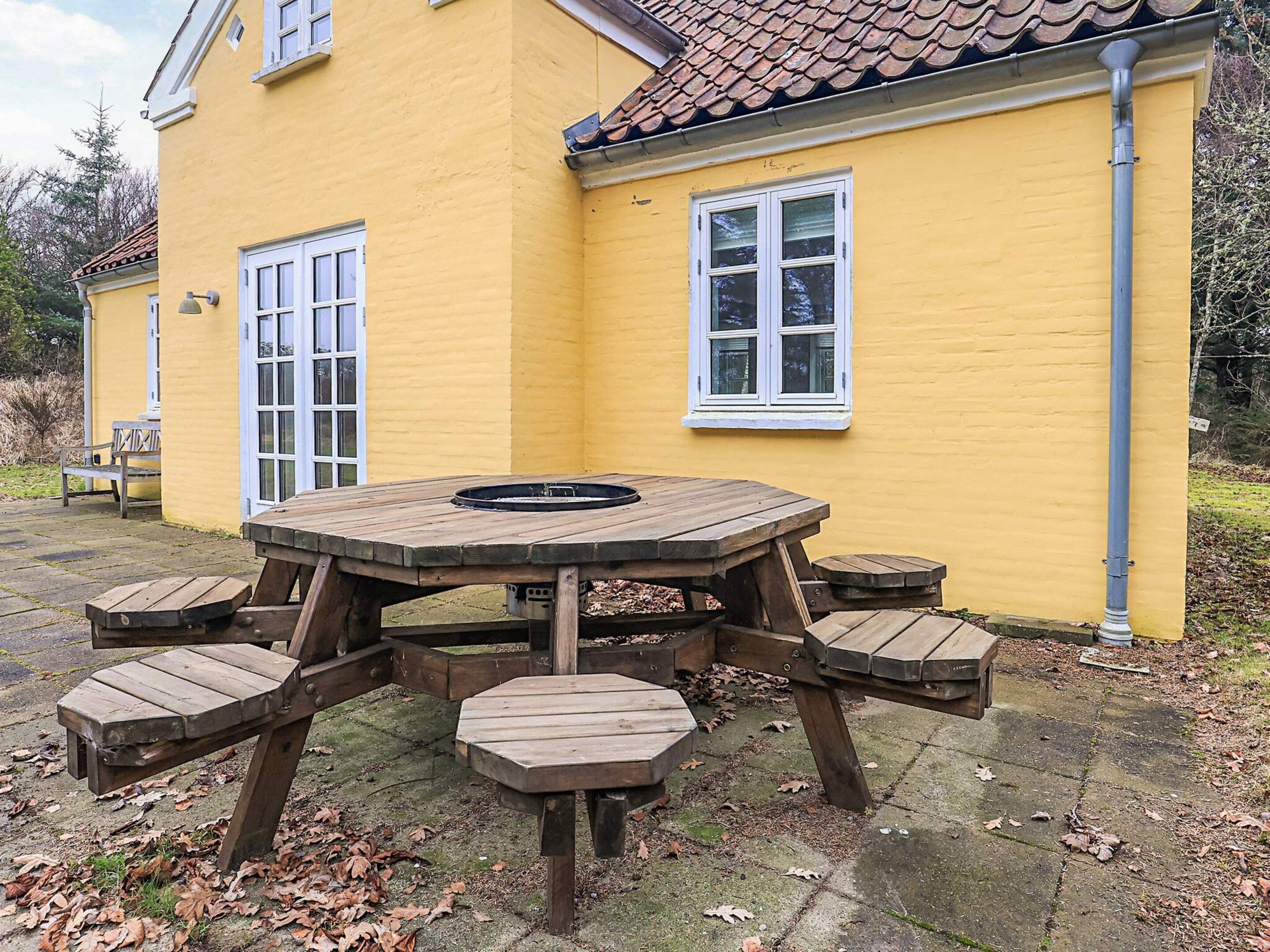 Ein gelbes Haus mit einem Ziegeldach, einem Holztisch mit Bänken und einem Fenster mit weißen Rahmen.