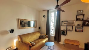 Ein Wohnzimmer mit einer Couch, einem kleinen runden Tisch, einem Deckenventilator und einem Fenster mit Vorhängen.