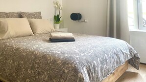 Ein Schlafzimmer mit einem Bett, einem Deckenventilator, einem Fenster mit Vorhängen und einem an der Wand montierten Lautsprecher.