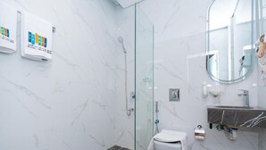 Ein modernes Badezimmer mit einer gläsernen Duschkabine, einer marmorverkleideten Wand, einer weißen Toilette und einem Waschbecken mit Marmorplatte.