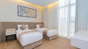Ein Hotelzimmer mit zwei Betten, einem Nachttisch, einem Schreibtisch und einem großen Fenster mit Vorhängen.