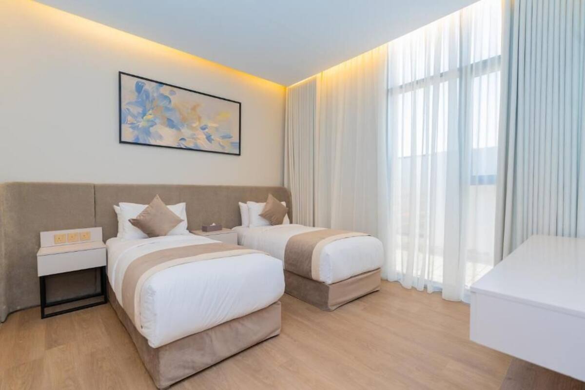 Une chambre d’hôtel avec deux lits, une table de chevet, un bureau et une grande fenêtre avec des rideaux.