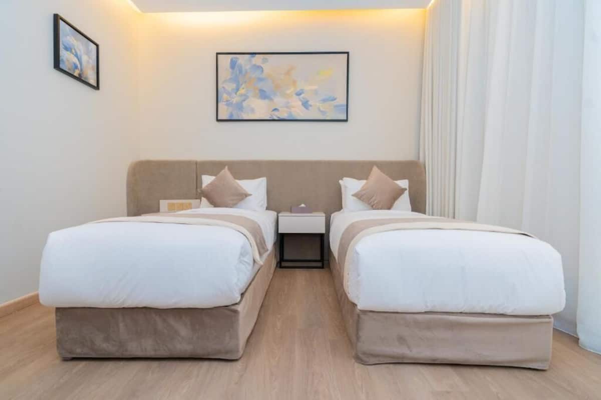 Une chambre avec un lit double, deux tables de chevet, une tête de lit et un tableau abstrait encadré accroché au mur.