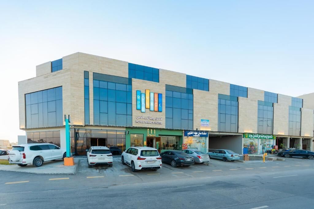 A modern hotel with a prominent sign, multiple parking spaces, and a storefront with a green awning.