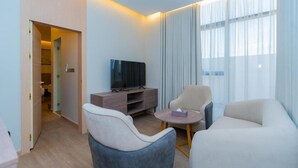 Ein modernes Hotelzimmer mit Fernseher, einer Couch, einem Sessel und einem kleinen runden Tisch.