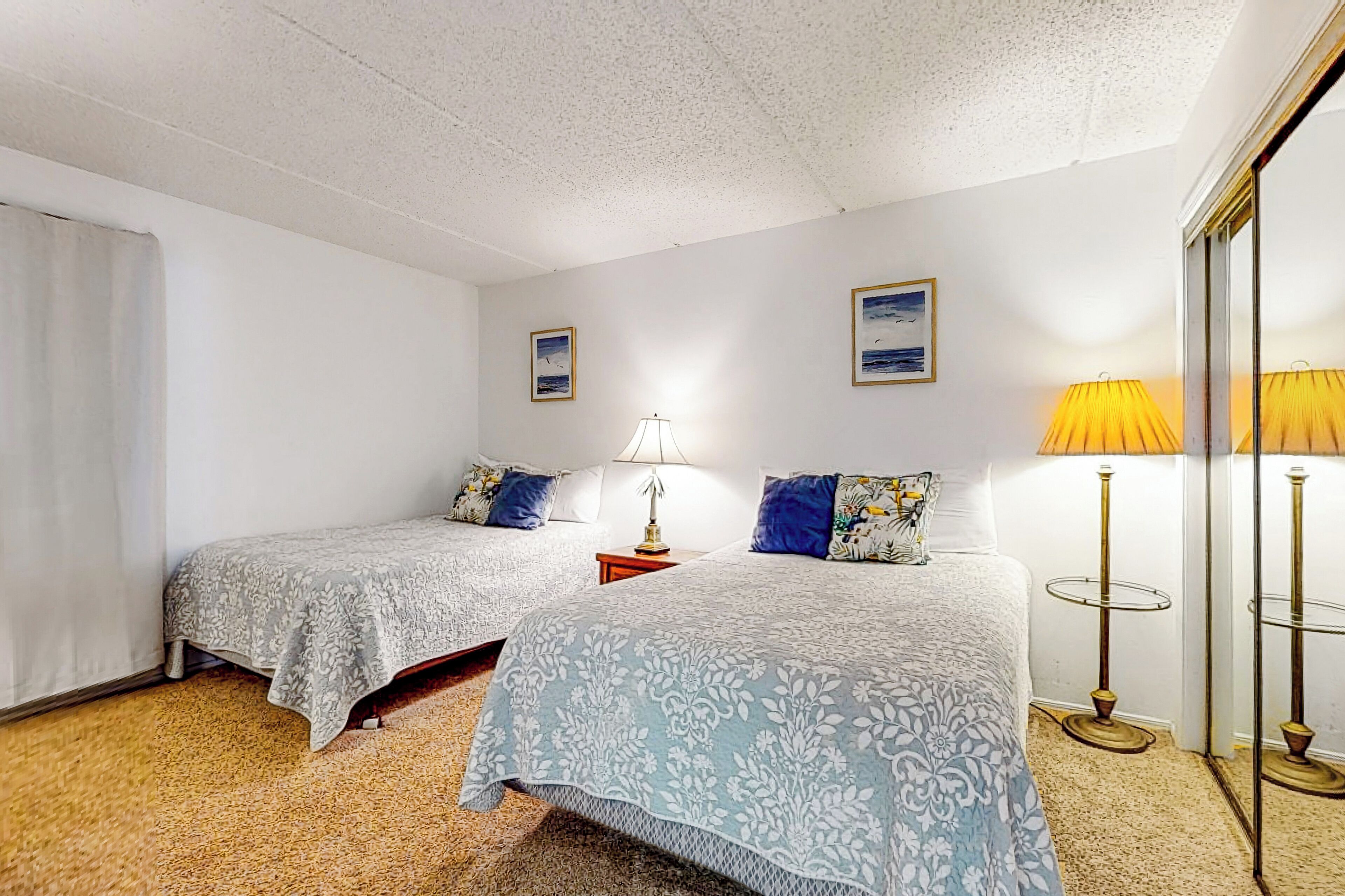 A hotel room with two beds, a small table, a lamp, and a mirror.