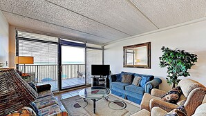 A living room with a sofa, armchair, coffee table, TV, and a balcony with a view. - Gulf-view Resort Retreat: Suntide III - Unit 209 (South Padre Island)