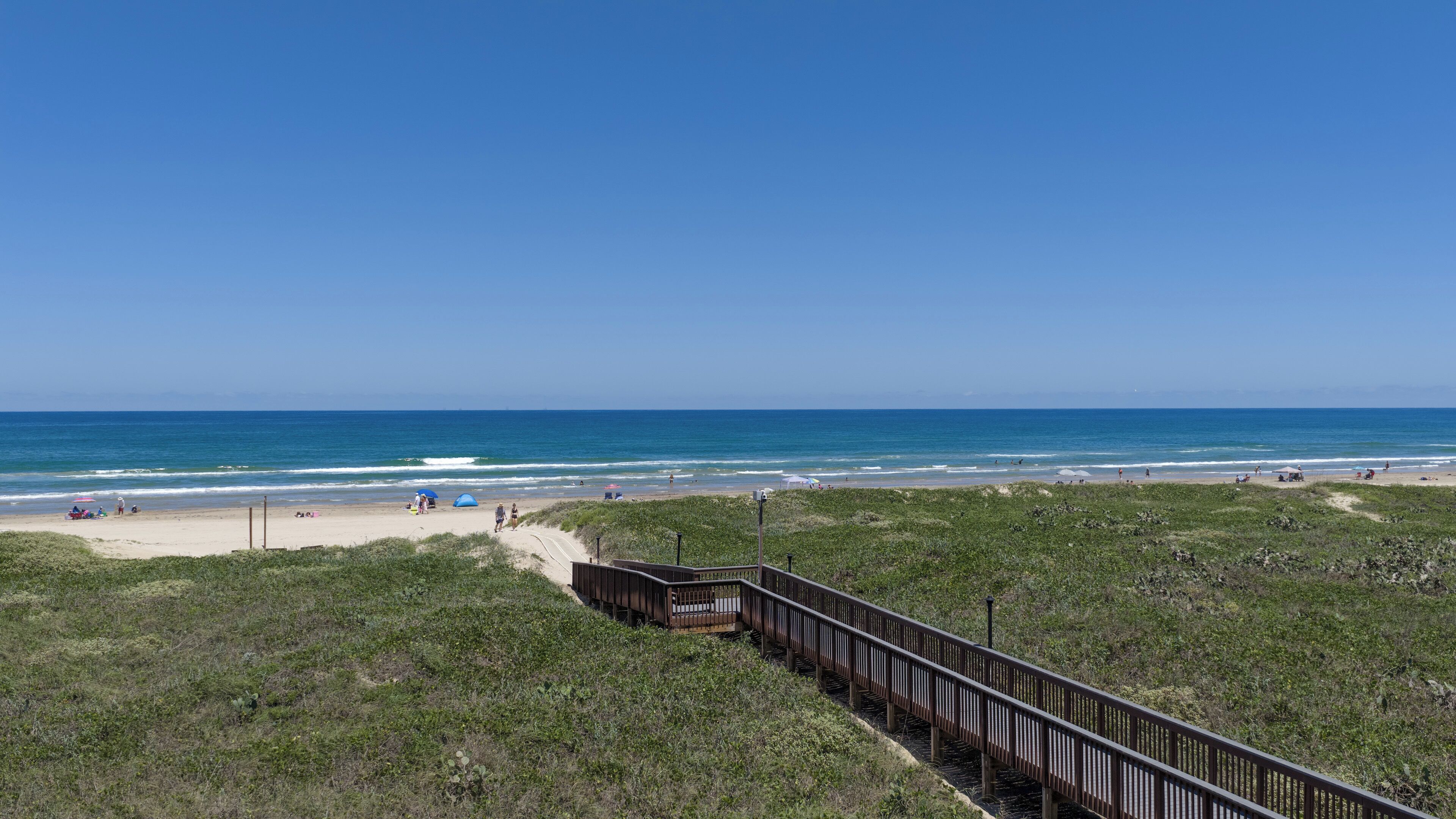 A beach with a wooden boardwalk leading to the shore, grassy dunes, and the ocean.