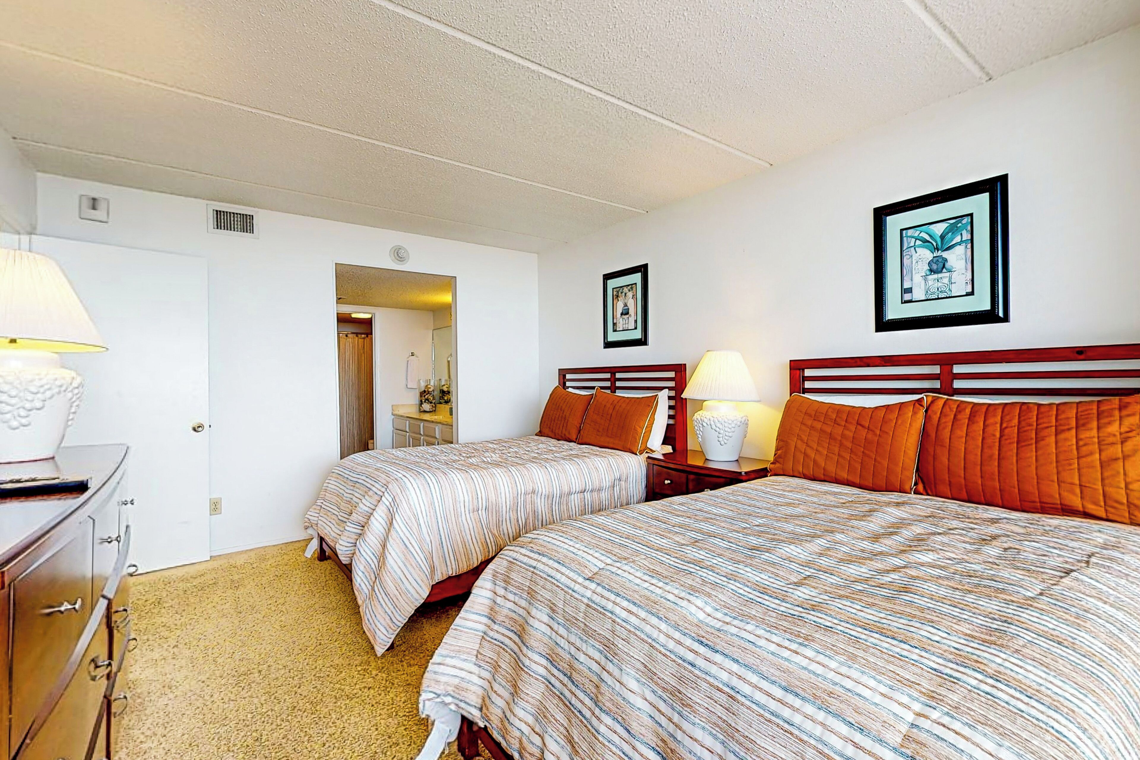 Une chambre d’hôtel avec deux lits, une commode, une lampe et un tableau encadré au mur.