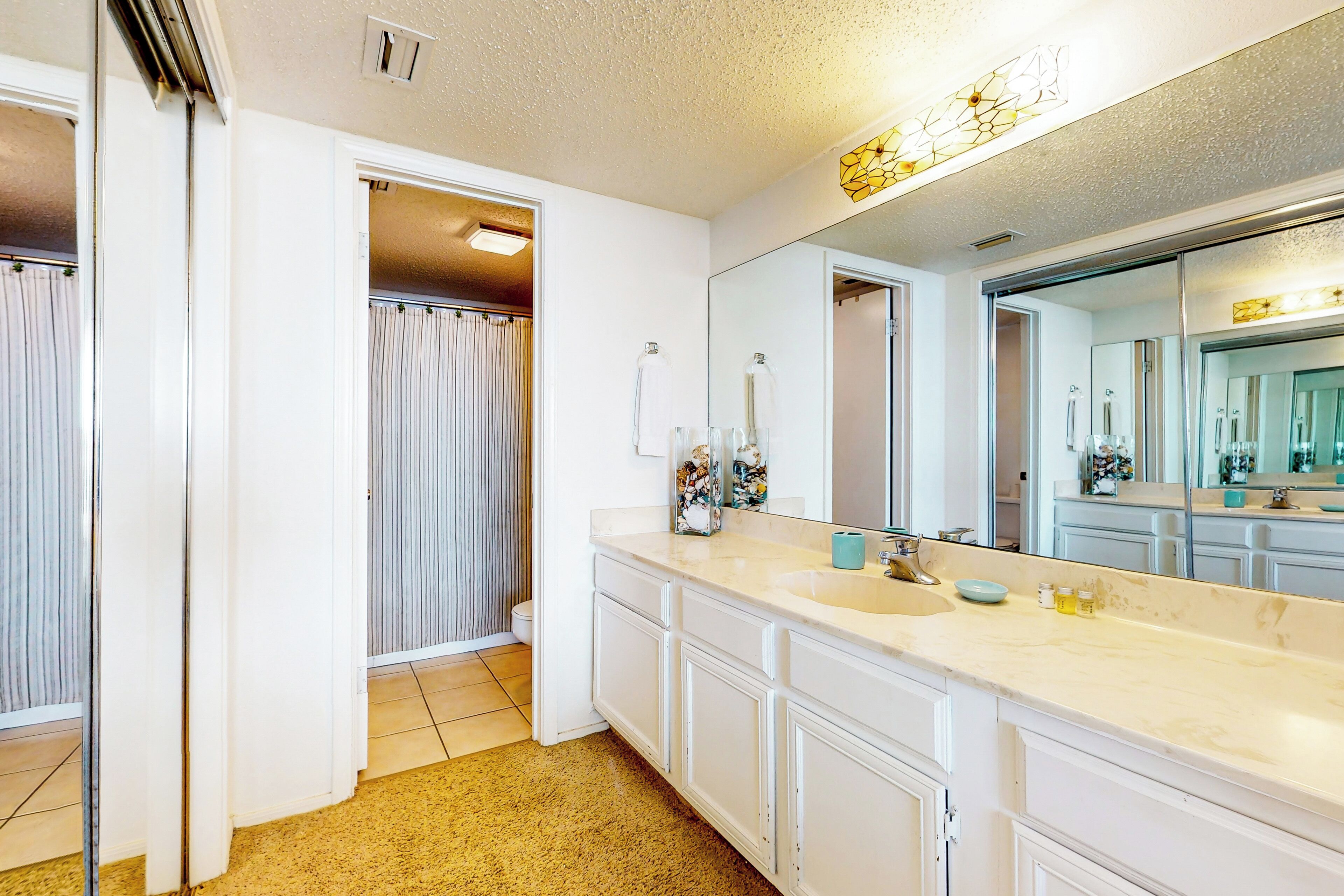 A bathroom with a large mirror, white cabinets, a sink, and a shower area.