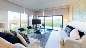 Een ruime woonkamer met een bank, fauteuils, een salontafel en een televisie.