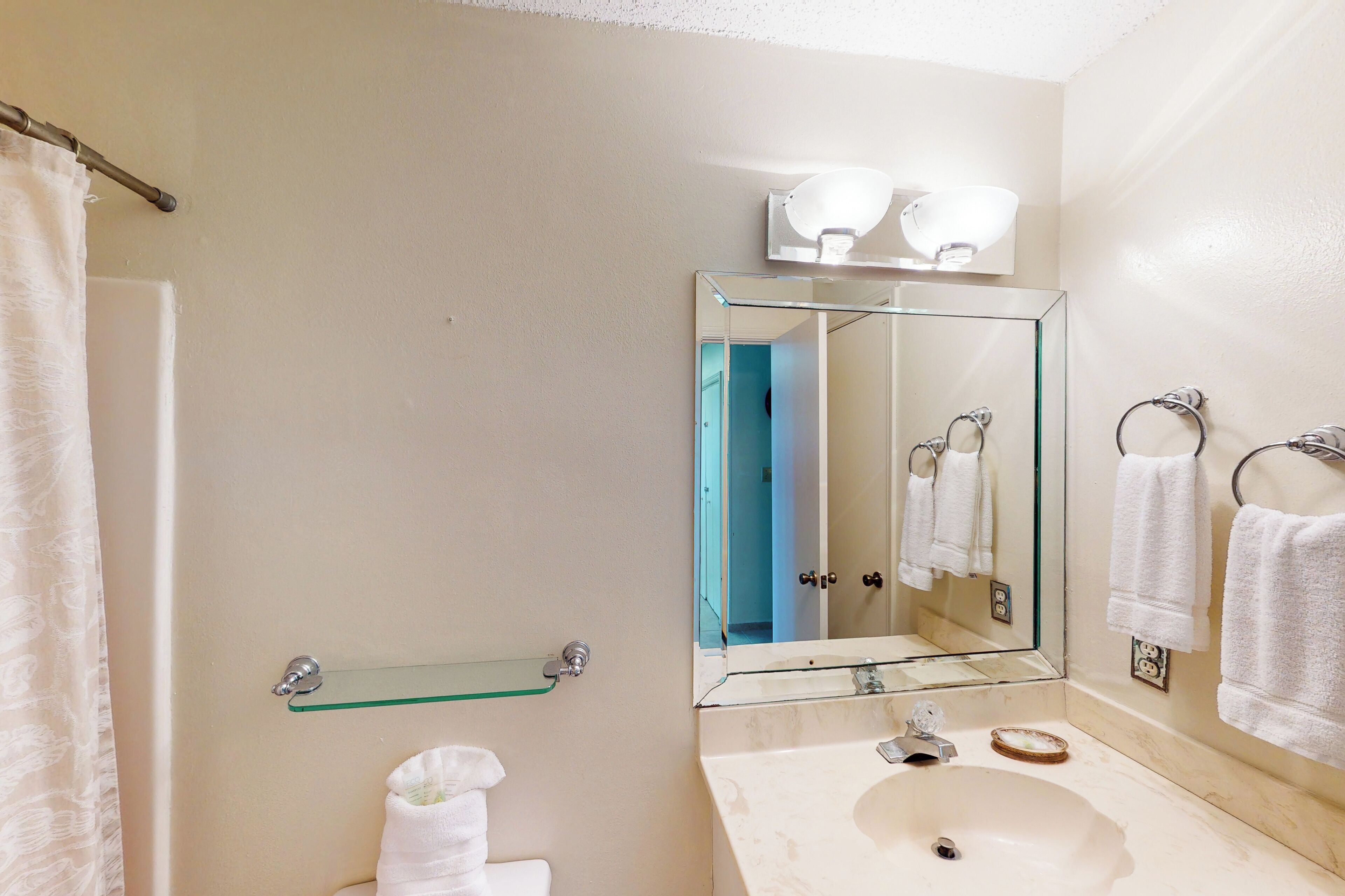 A bathroom with a glass shelf, a sink, a mirror, and a towel rack.