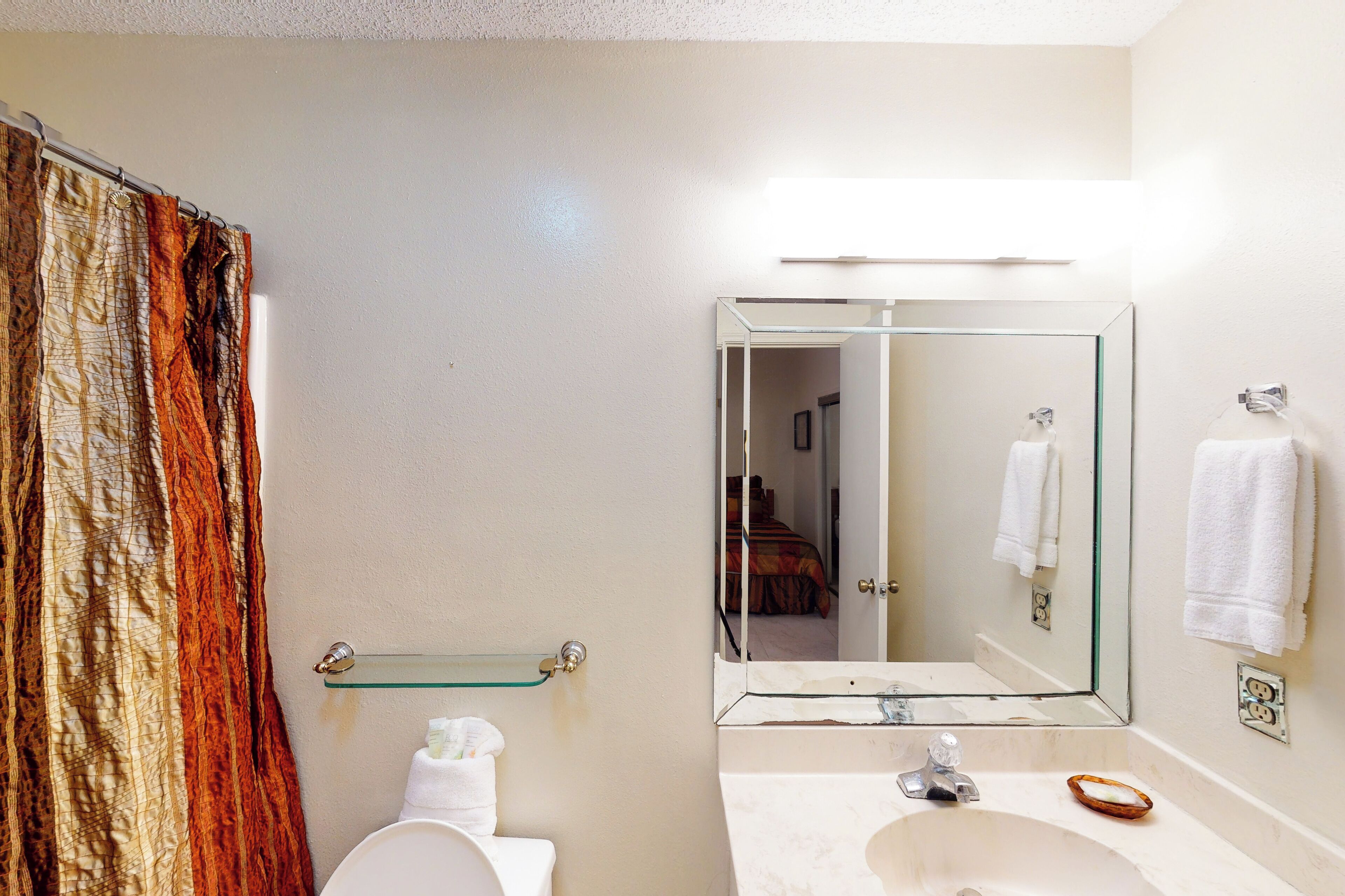 A bathroom with a toilet, sink, mirror, and shower curtain.
