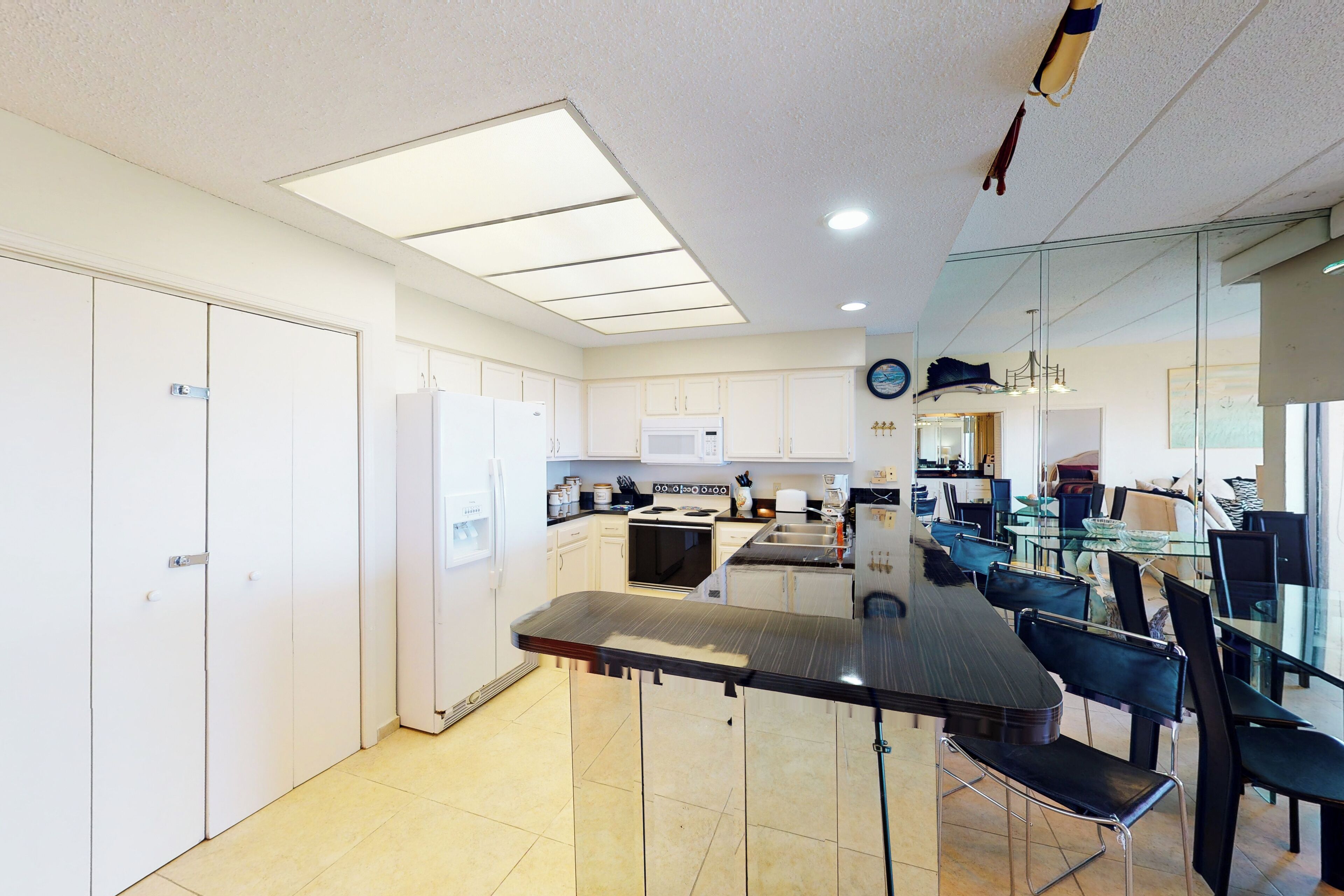 Una cocina moderna con armarios blancos, una isla central y un comedor con sillas negras.