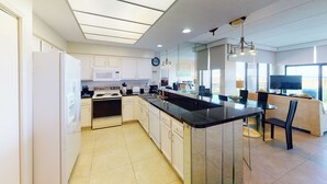 Een moderne keuken met een centraal eiland, witte kasten en een zithoek met een bank en stoelen.
