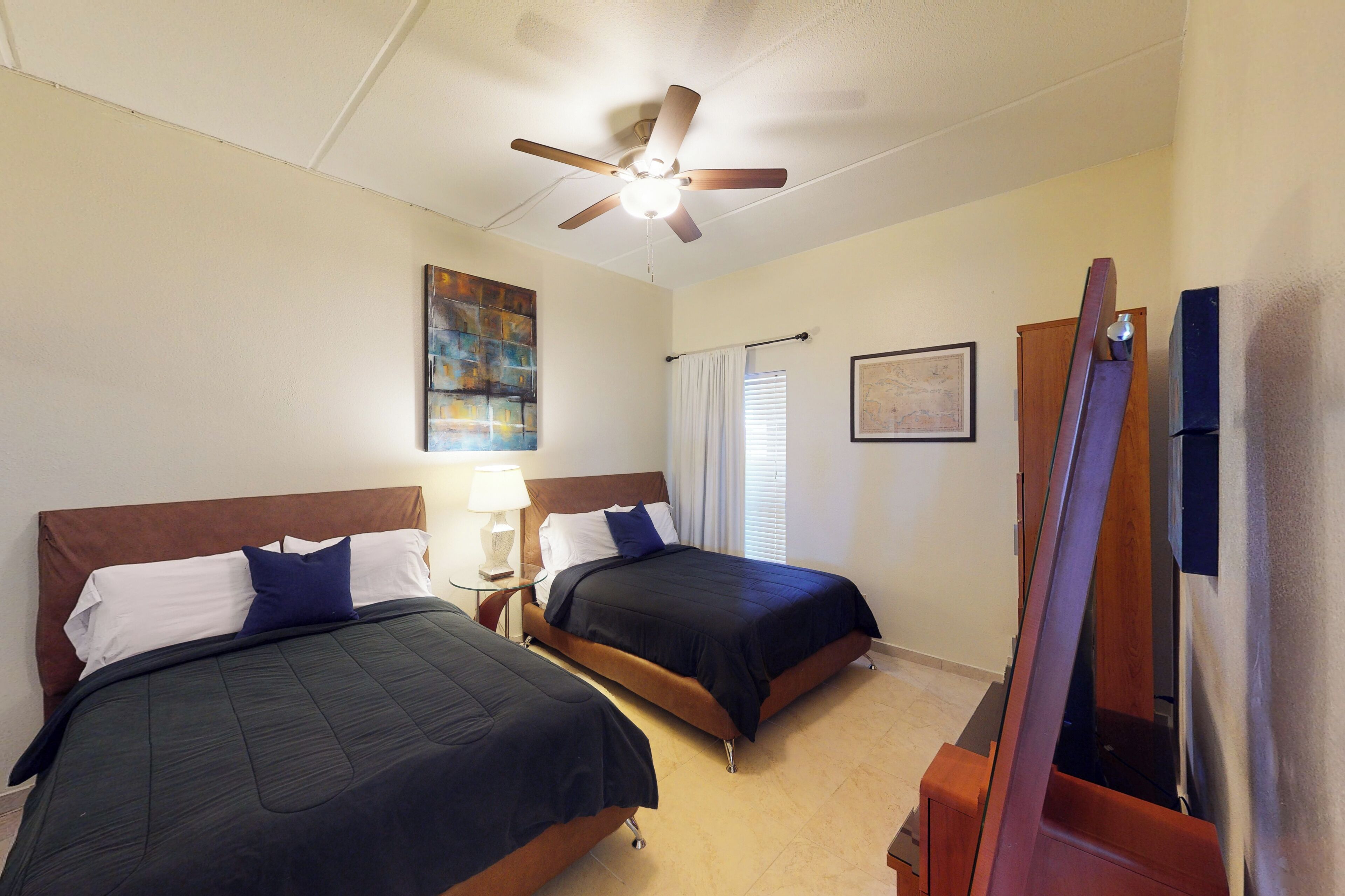 A hotel room with two beds, a ceiling fan, a painting, a lamp, and a television.