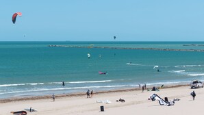 Een strand met mensen, een pier en een heldere lucht.